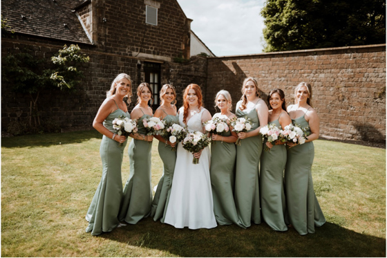 Bride and bridesmaids holding bouquets stand on grass